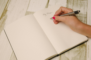 person writing a heading in a blank book: My Plan
