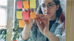 person arranging sticky notes on a glass wall