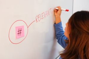 woman writing the word "relevant" at white board with sticky note circled