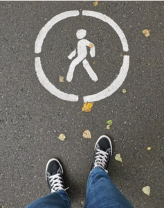 person's feet in sneakers, standing on pavement next to a walk icon