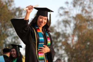 woman in graduation regalia, holding up a diploma