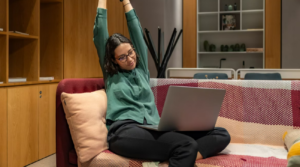 woman on couch with laptop, stretching and flexing her arms above her head