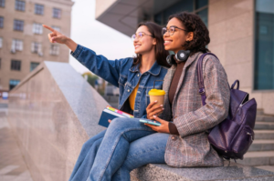 two college students sitting outside; one is pointing to something