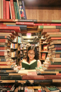 woman reading books in a library, framed by a circle of stacked books