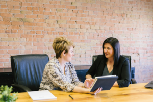 two women working together at a table, with a laptop