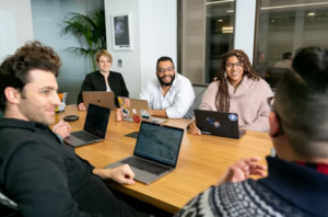 employees with open laptops sitting around a table in an office