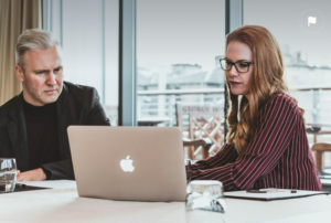 two people at a table, looking at a laptop screen