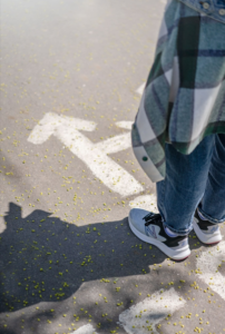 person standing on pavement with arrows on the pavement showing different directions