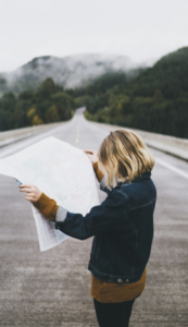 person holding roadmap and standing in road that goes into the distance